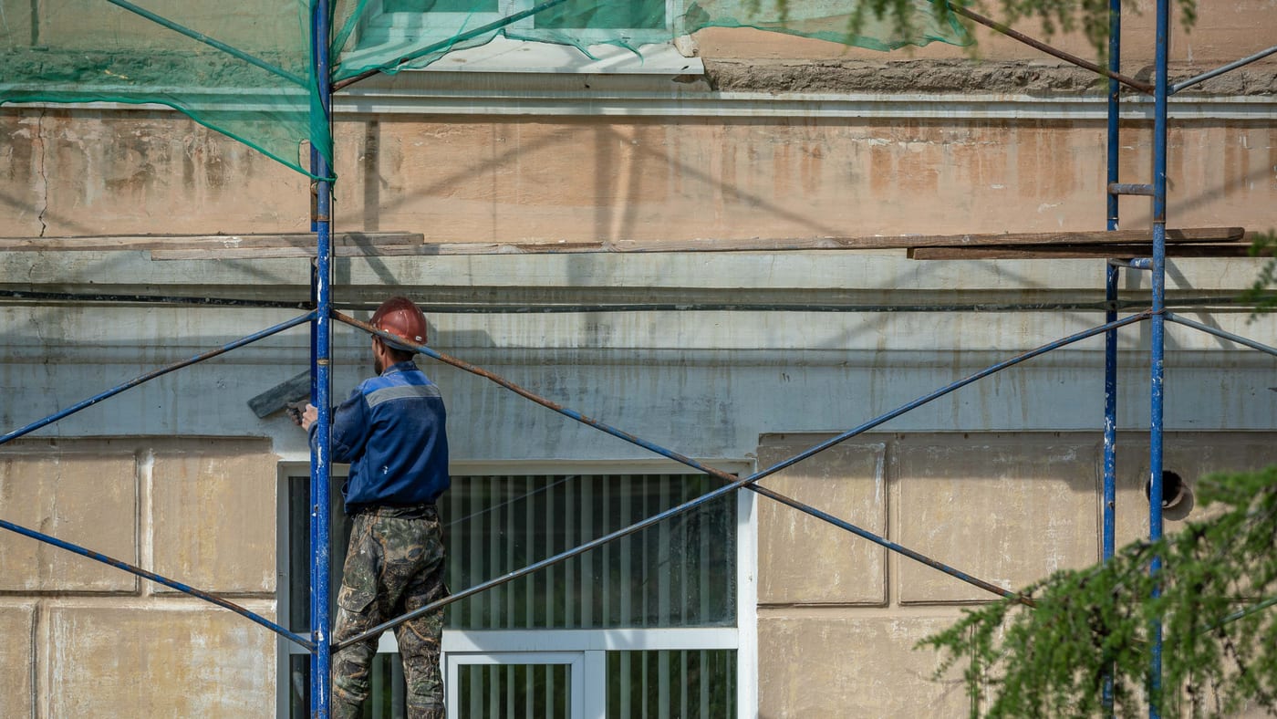 Ouvrier sur échafaudage traitant la façade d'un bâtiment lors de travaux de rénovation énergétique