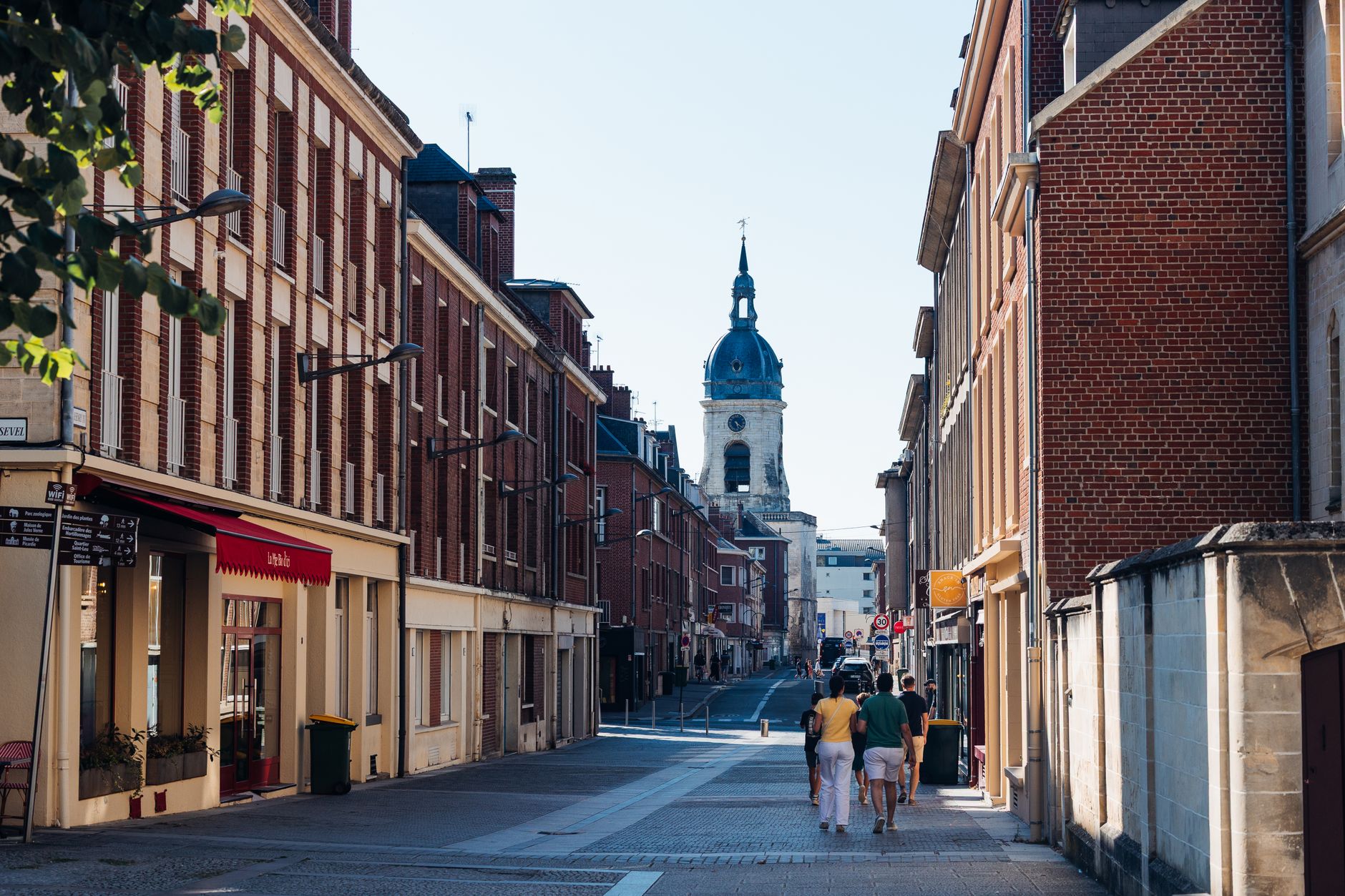 Rue bordée d'immeubles en brique rouge à Amiens, beffroi en arrière-plan